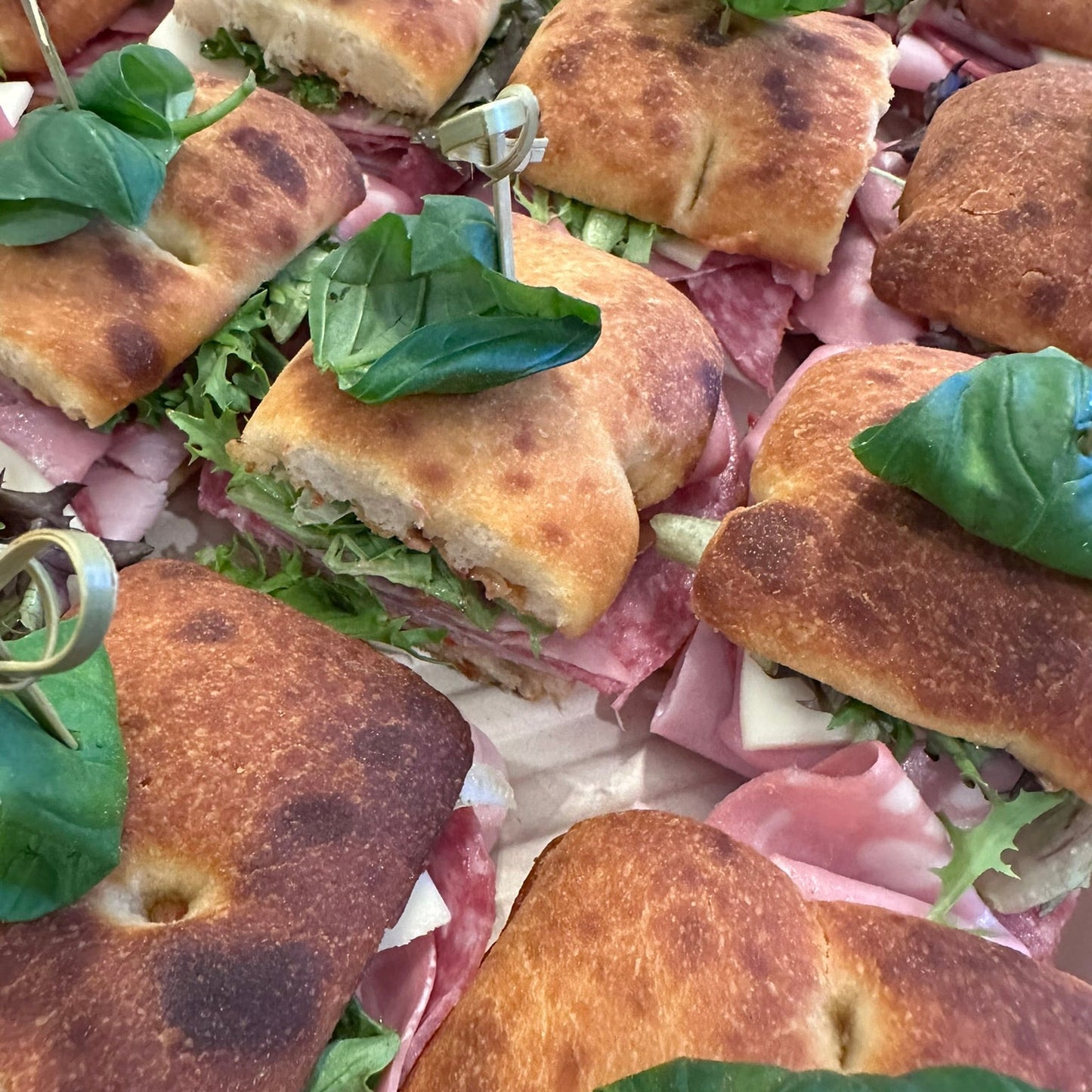 Close-up of small sandwiches with bread, ham, and lettuce on a plate.