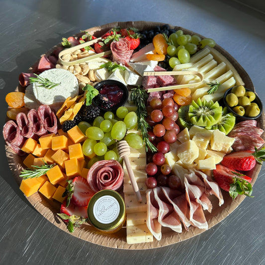 Assorted charcuterie board with meats, cheeses, fruits, and vegetables on a wooden board.