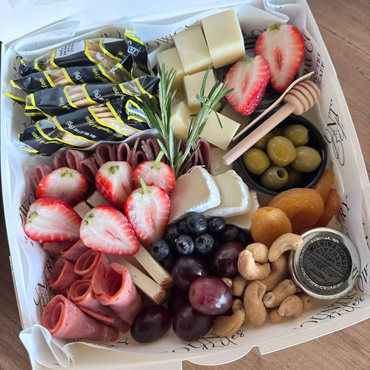 Assorted charcuterie board with meats, cheeses, fruits, and nuts in a white box.