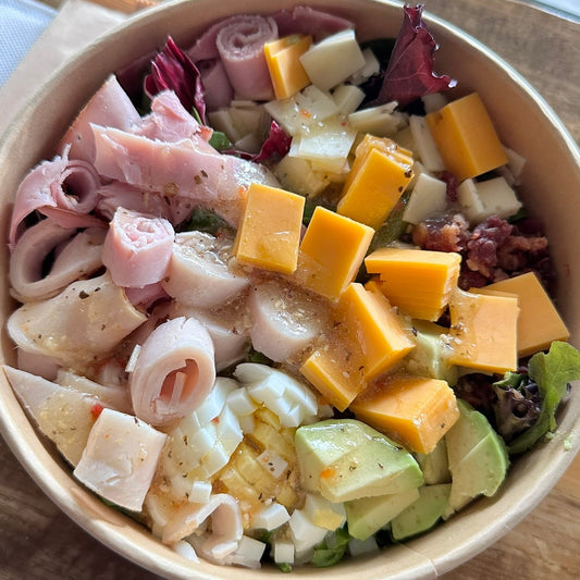 Salad with cheese and meat in a paper bowl on a wooden table