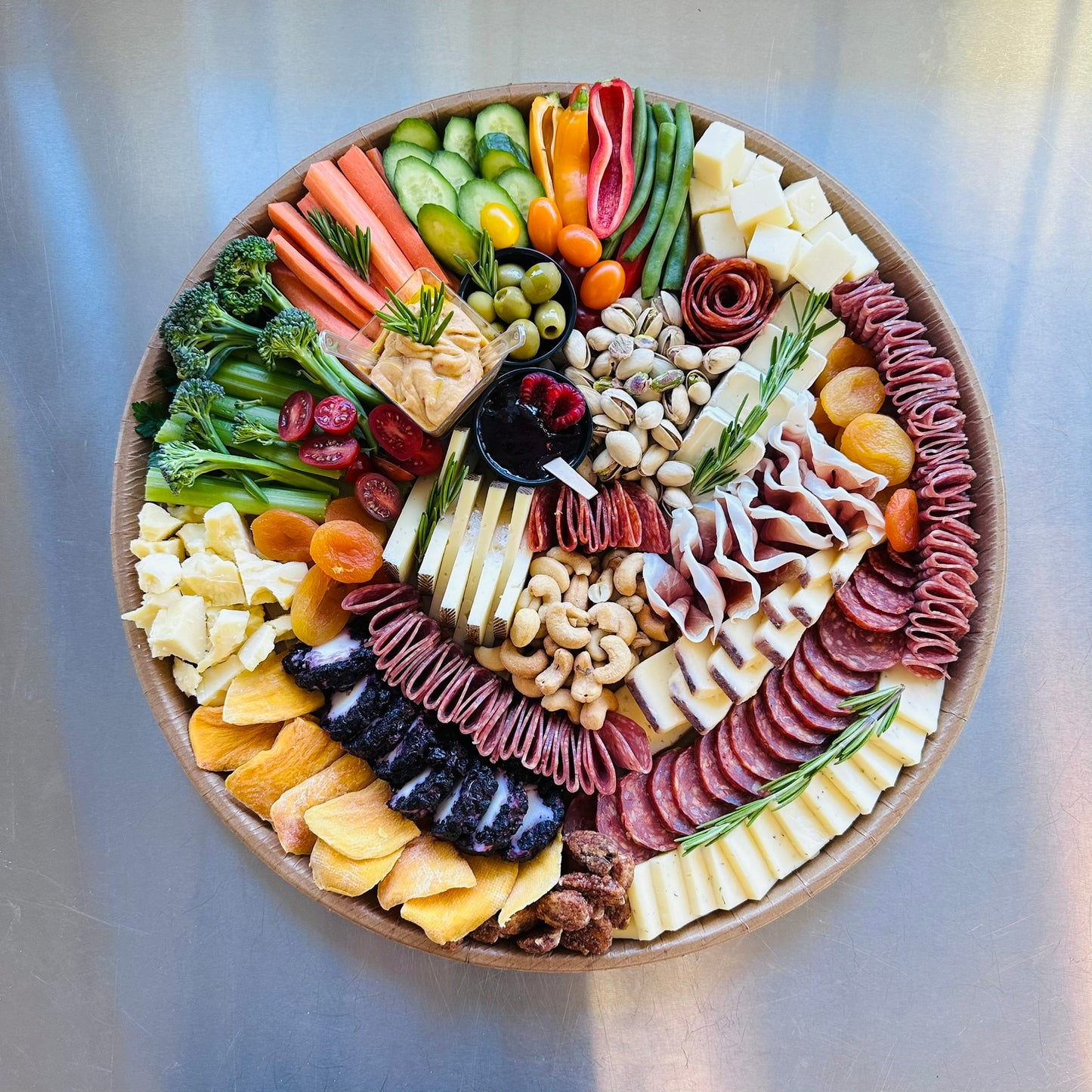 Assorted meats, cheeses, and vegetables arranged in a circular platter on a metallic surface.